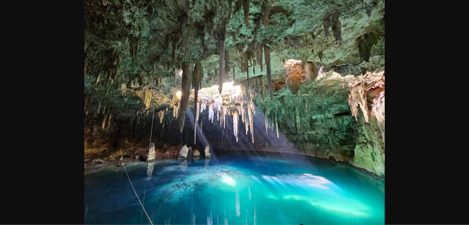 Lush tropical cenote with hanging jungle vines and turquoise crystal clear water near Chichen Itza